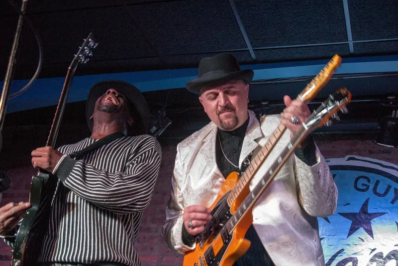 A Chicago blues band on a club stage, guitar, harmonica and drums.