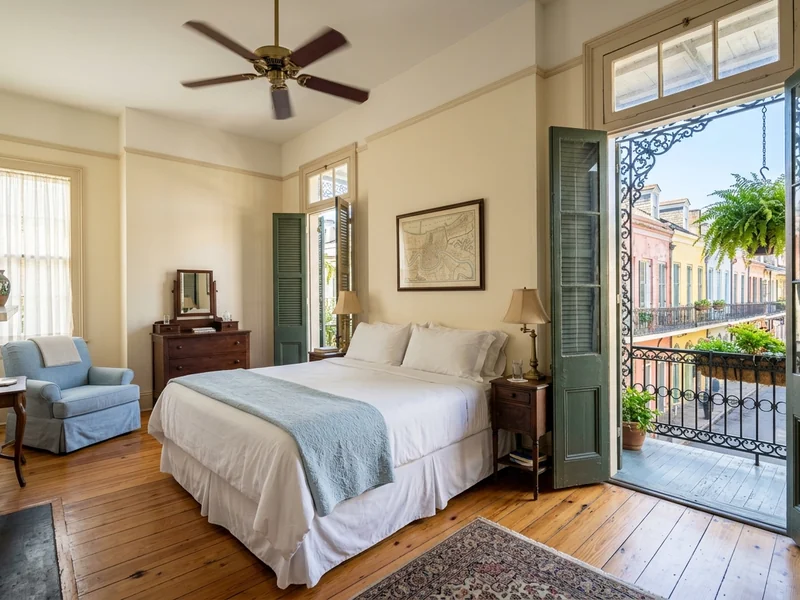 A French Quarter hotel room in New Orleans with a double bed and an iron balcony.