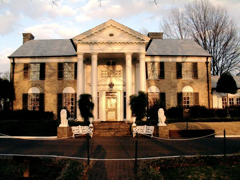 The white columned front of Graceland, Elvis Presley's home in Memphis, behind a green lawn.