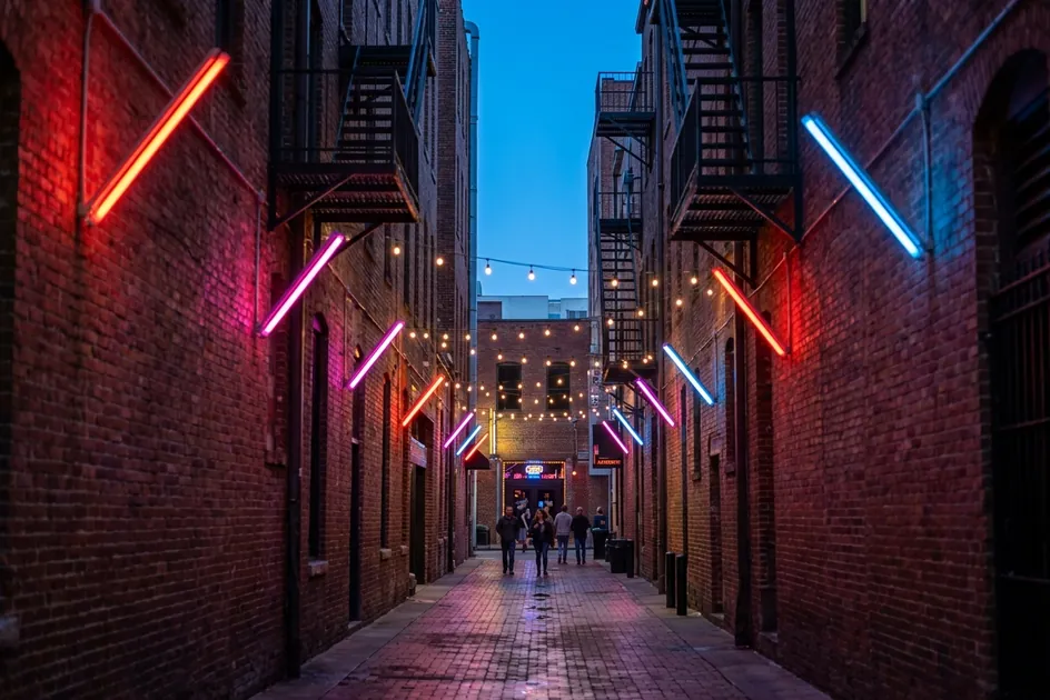 Printers Alley in downtown Nashville at blue hour, a brick lane lit by neon signs.